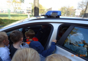 Dzieci z bliska ogladają radiowóz policyjny.